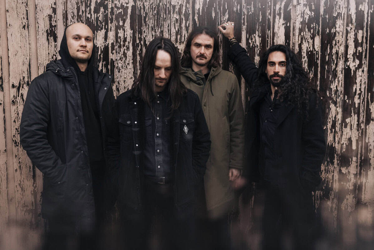 Four men in dark jackets pose against a peeling wooden wall, creating a moody band portrait.