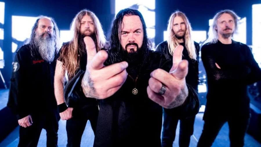 Hard rock/metal band posing together, with the frontman pointing at the camera, intense stage lights behind them.