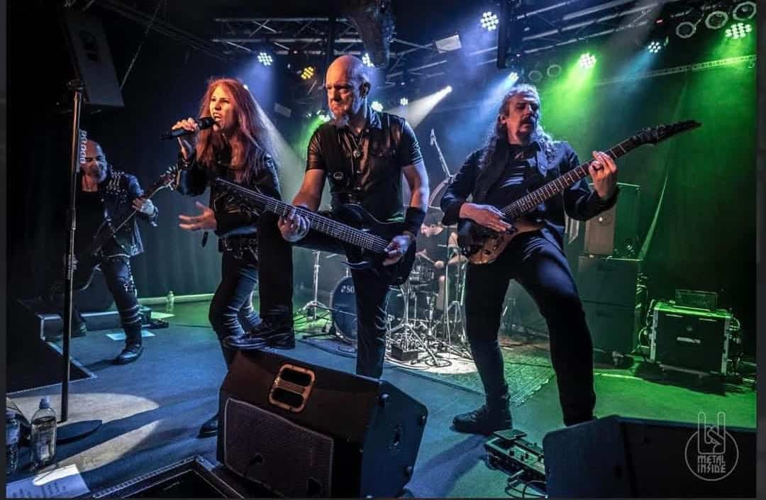Rock band performing on stage with a female vocalist and two guitarists under colorful stage lights.