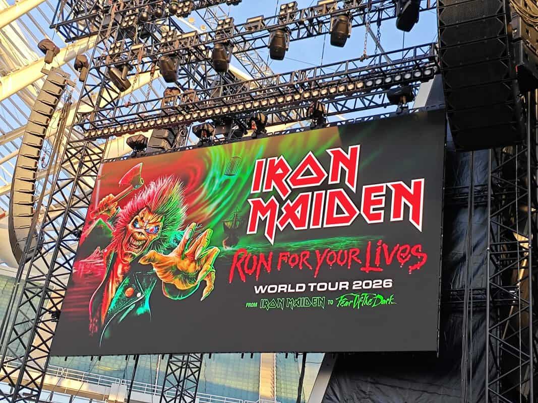 Large stage screen displaying Iron Maiden Run for Your Lives World Tour 2026 graphic with a neon-green monster reaching forward and bold red lettering, rigging above.