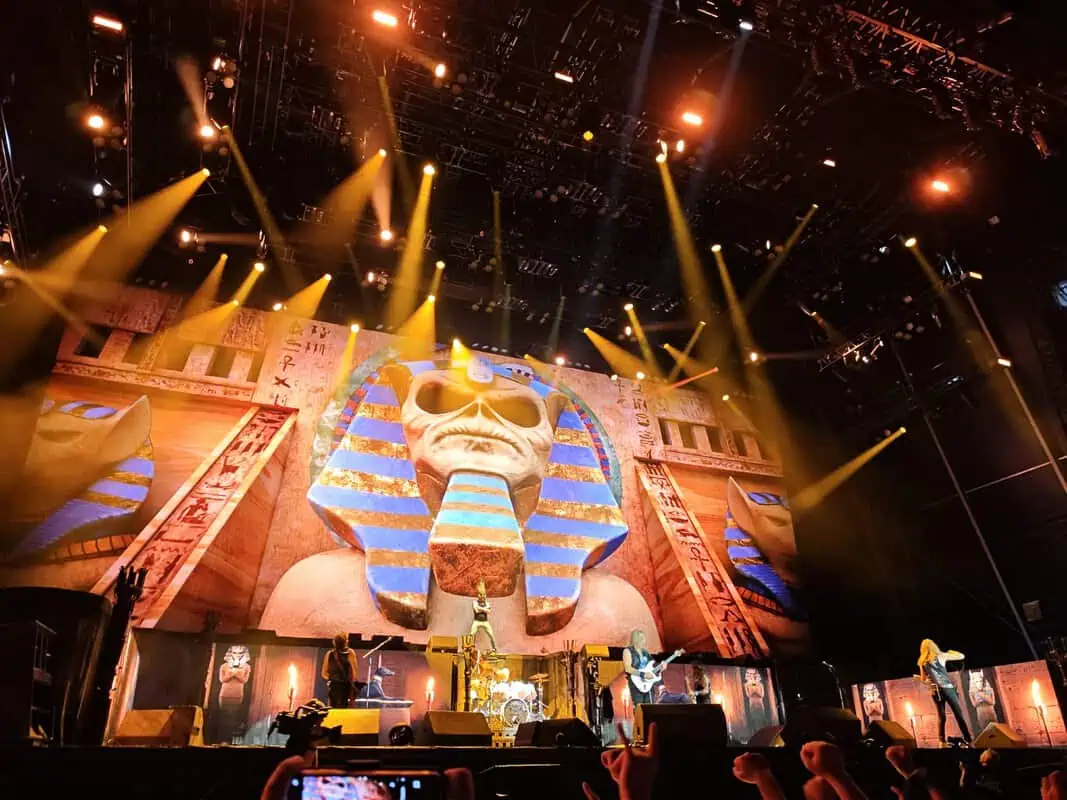 Concert stage with a giant Egyptian sphinx banner and a band performing under orange lights at a live show.