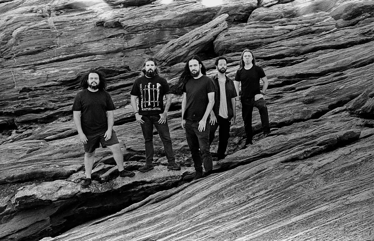 Five men stand together on a steep, layered rock formation outdoors, facing the camera in a group photo.