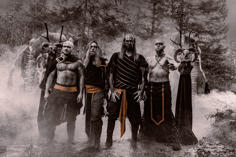 Six men in black and orange fantasy costumes pose in a smoky forest clearing, wearing armor-like belts and cloaks.