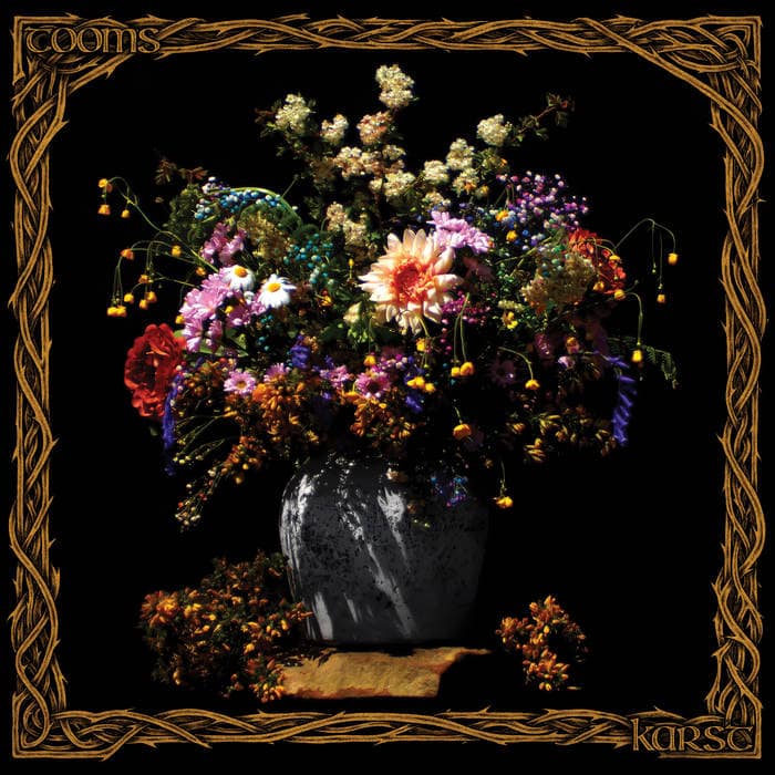 Colorful bouquet of flowers in a dark ceramic vase on a wooden pedestal, set against a black background and framed with an ornate gold border.