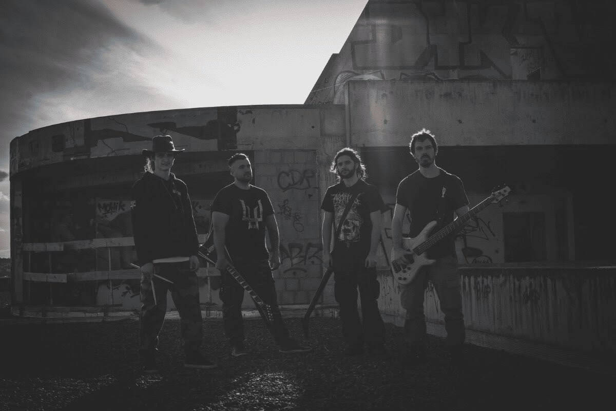 Four musicians stand with guitars on a graffiti-covered rooftop, posing for a photo in dim light.