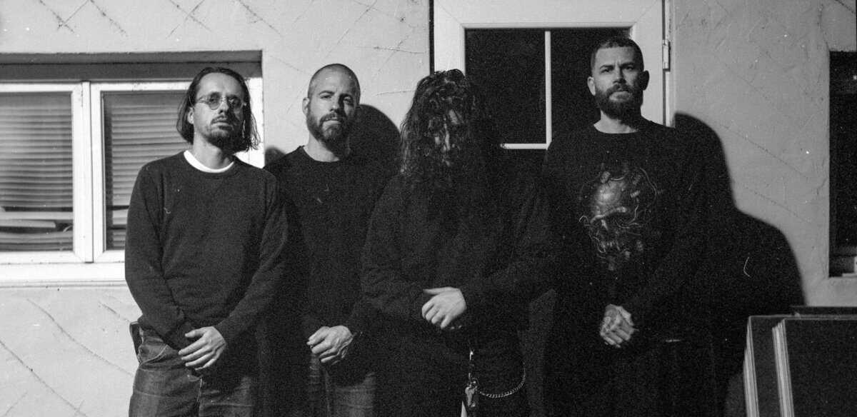 Five men in dark clothing stand in a doorway outside a building; black-and-white group photo.