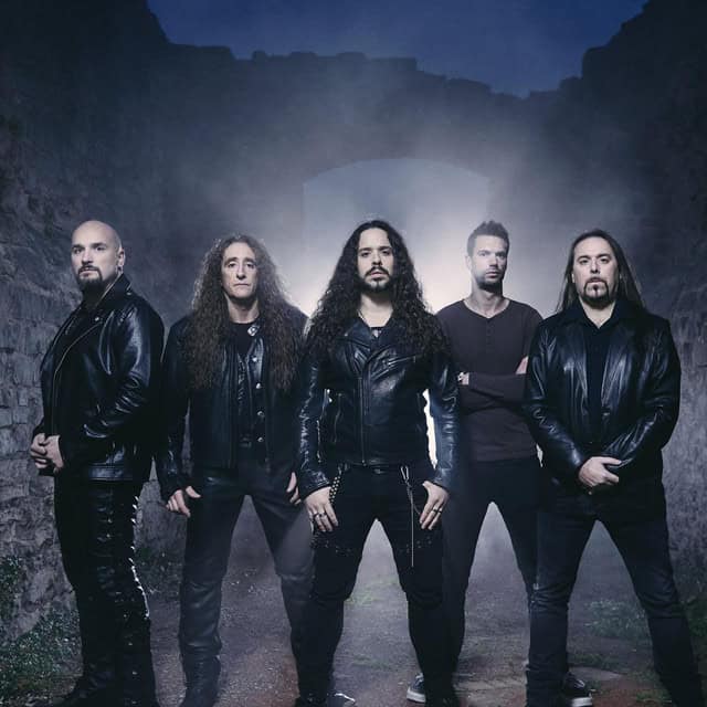Five men in black leather jackets stand in a foggy, tunnel-like stone arch, posing for a band portrait.
