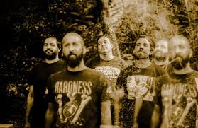 Six men stand in a wooded area wearing dark band T-shirts, posing for a moody outdoor group photo.