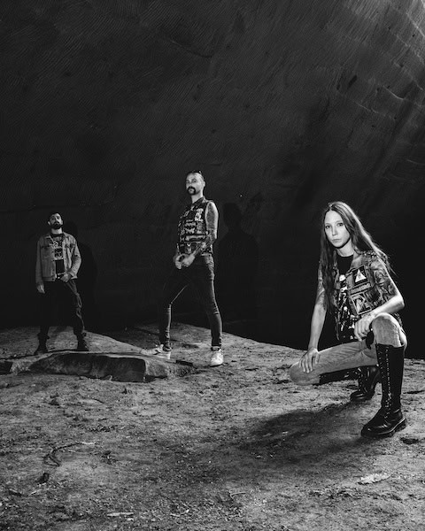 Black-and-white photo of three people on a rocky, cratered surface; a woman kneels at the right while two men stand behind in patched denim vests.