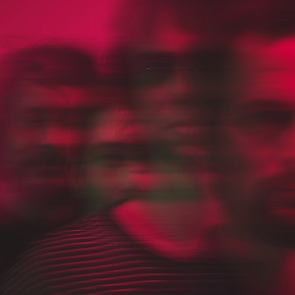 Abstract, red-tinted motion blur of indistinct figures in a crowded scene, conveying energy and movement.