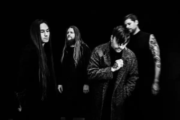 Black-and-white photo of a four-member rock band posing in dark clothing against a black backdrop.