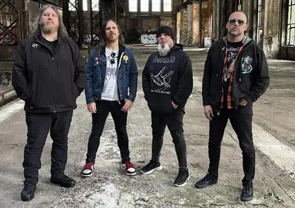 Four men in casual jackets posing in an empty, dilapidated warehouse, suggesting a rock band photo.