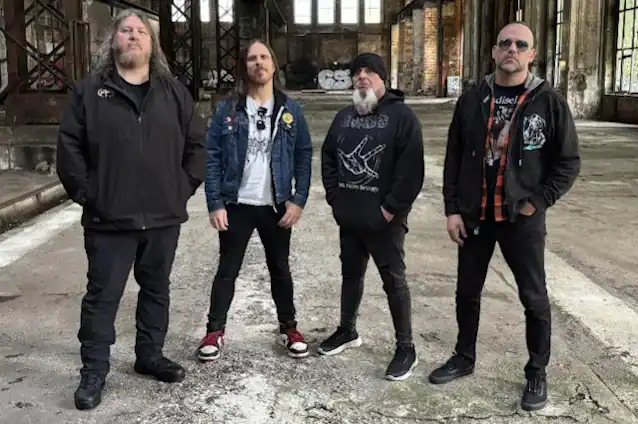 Four men in casual jackets posing in an empty, dilapidated warehouse, suggesting a rock band photo.