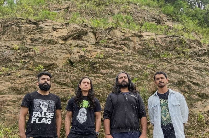 Four men stand side by side outdoors in front of a rocky dirt cliff.